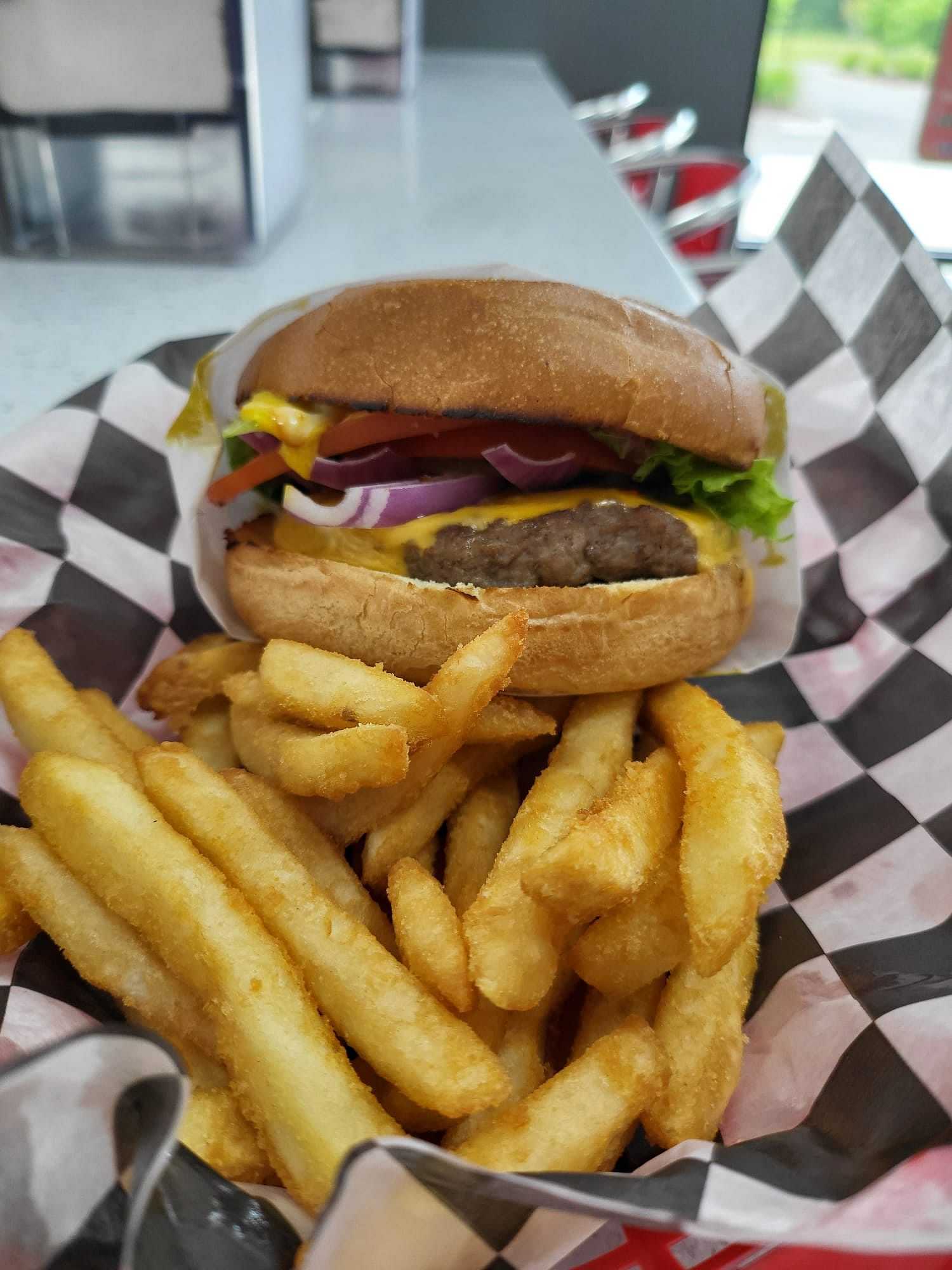 Burger with lettuce, cheese, tomato, and onions, served with crispy fries in a checkered basket.