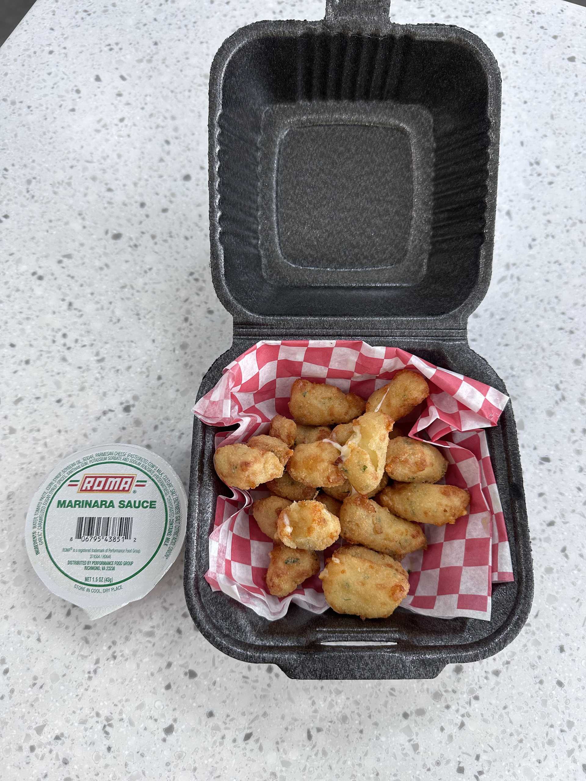 Fried cheese curds in a black takeout box with a side of marinara sauce on a speckled countertop.