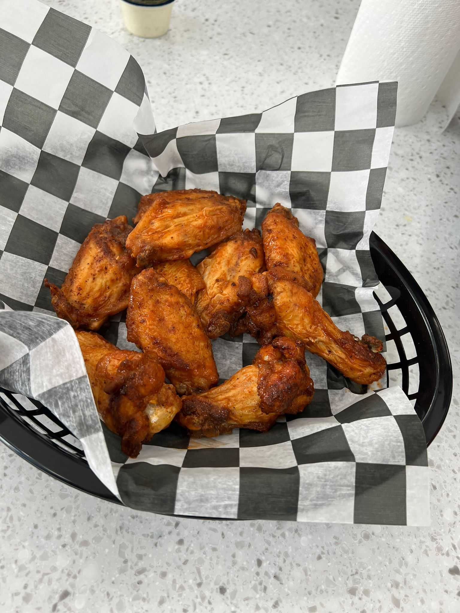 Basket of crispy, spicy fried chicken wings on a checkered paper-lined basket on a light countertop.