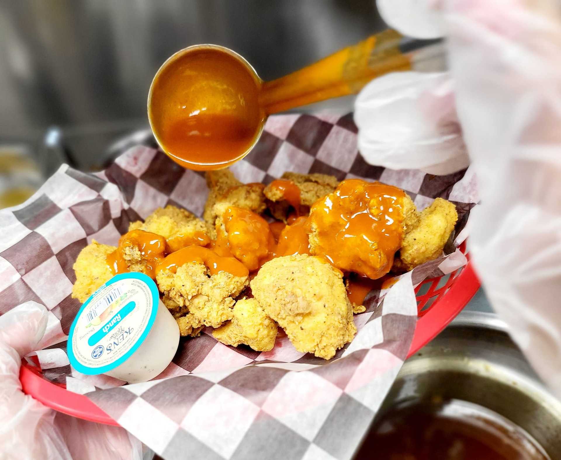 Chicken bites in a basket being drizzled with sauce, served with a side of dipping sauce.
