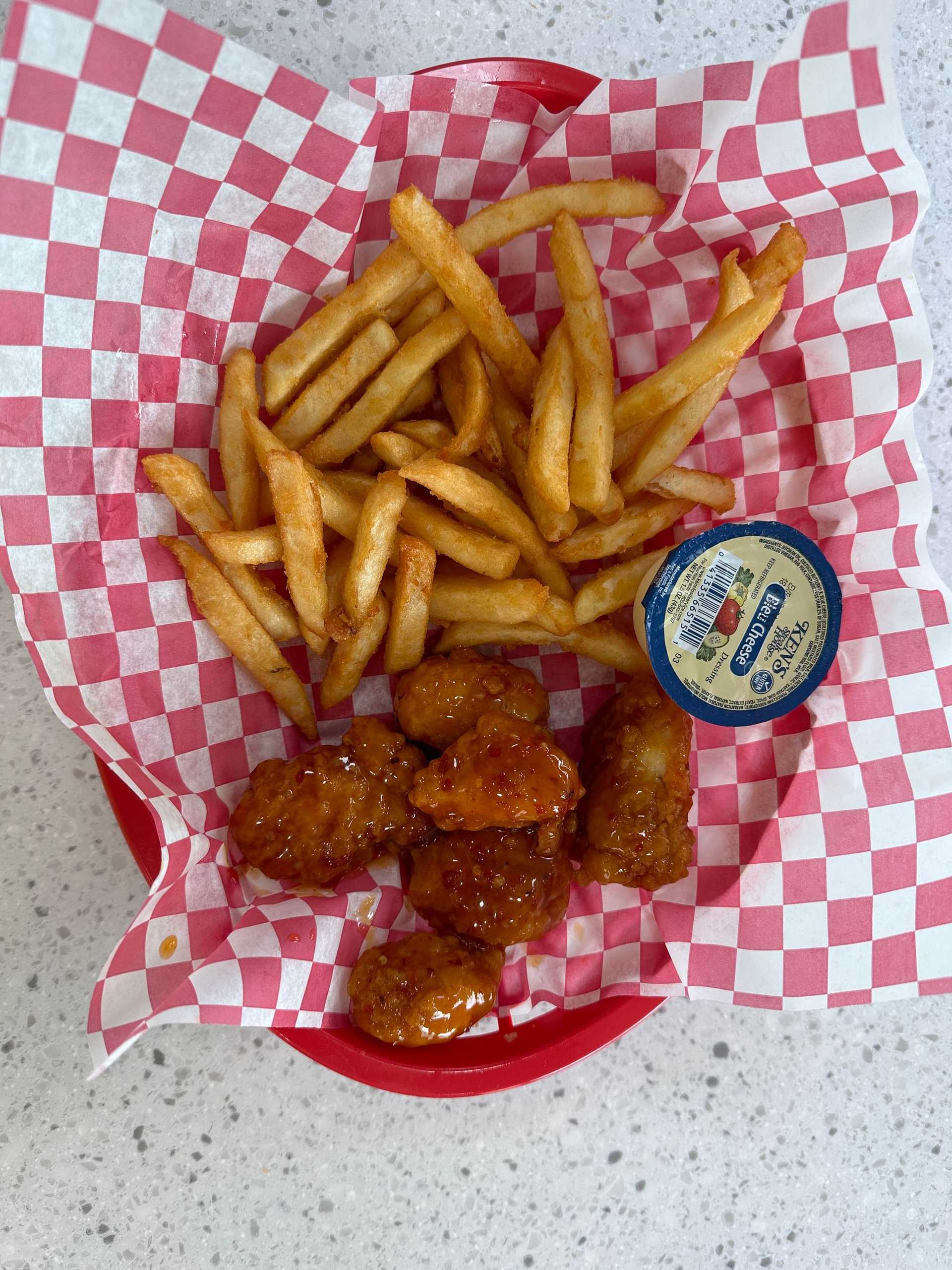 Basket of chicken nuggets with fries, red dipping sauce, on a checkered paper-lined tray.